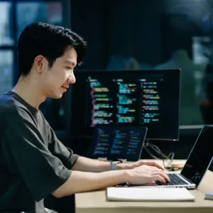 Web Developer coding with computer screens in the background.