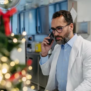 Business man answering phone with a Christmas tree in the background.